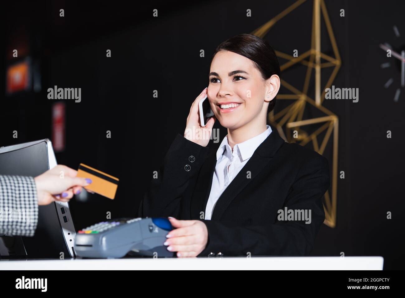 Der Rezeptionist lächelte und sprach mit dem Smartphone in der Nähe des Gastes mit Kreditkarte Stockfoto