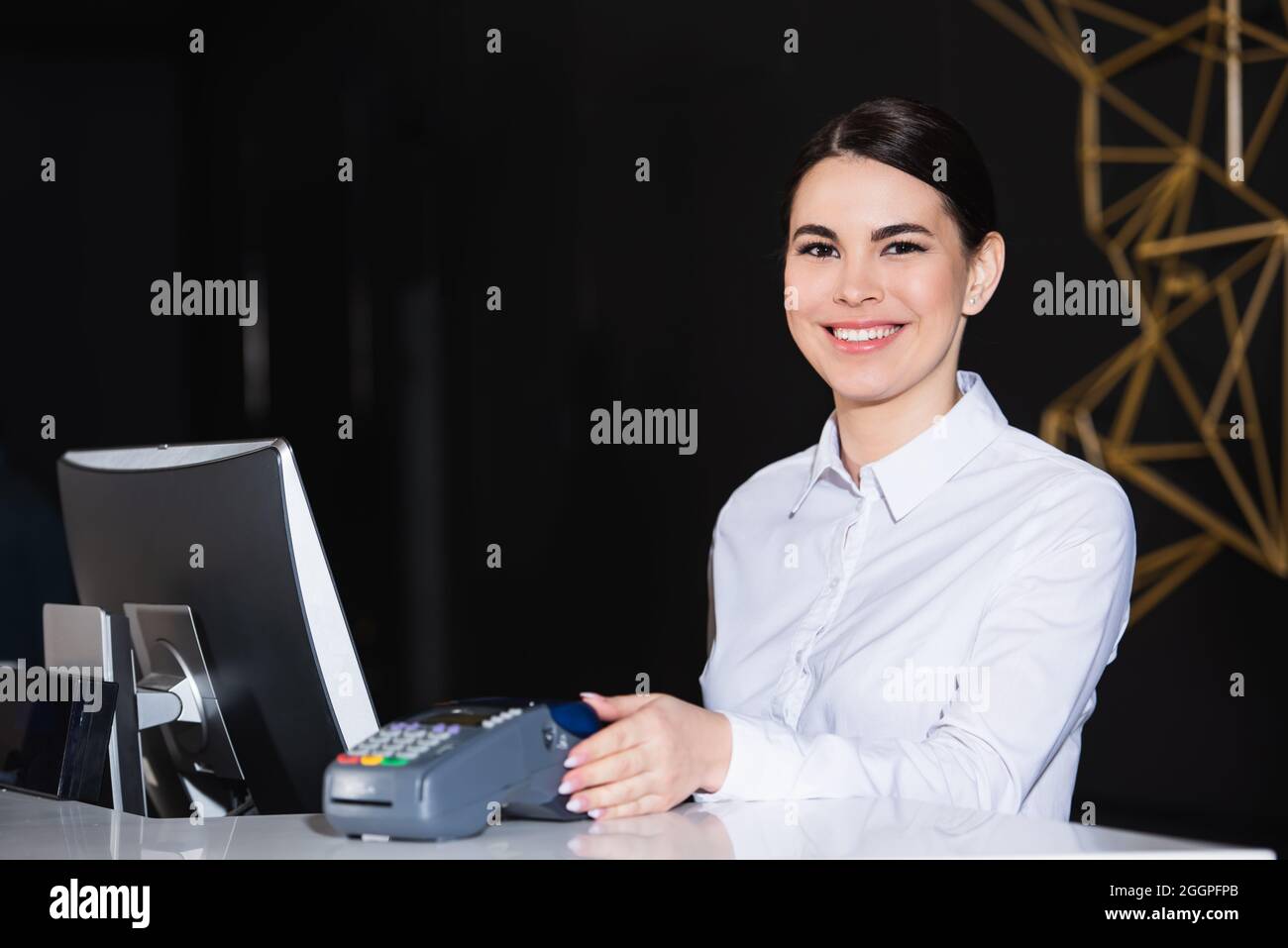 Der Rezeptionist lächelte freundlich neben dem Kreditkartenleser am Empfang Stockfoto