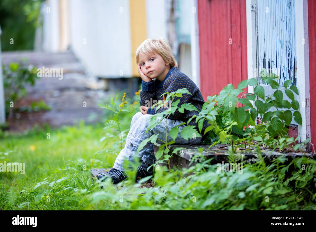 Trauriges kleines Kind, Junge im Vorschulalter, auf der Treppe vor dem alten zerstörten Haus sitzend, traurig und weinend Stockfoto