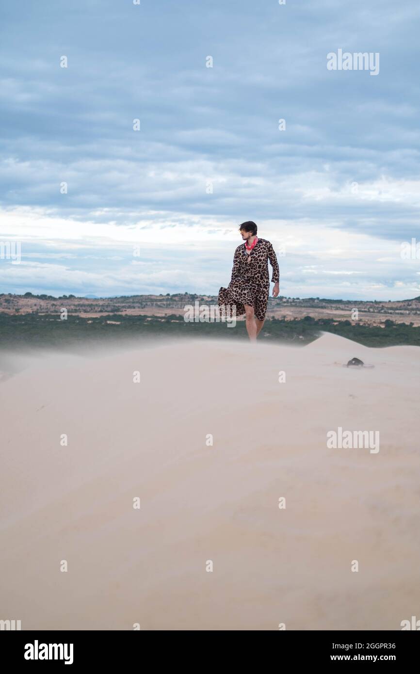 Wanderer beim Wandern in der Wüste. Junger Mann, der in weißen Sanddünen steht. Fremder in der Wüste. Sand fliegt im Wind. Kleidung flattert im Wind Stockfoto