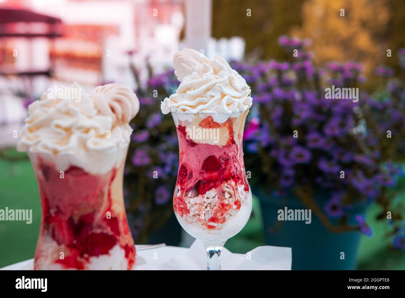 Erdbeereis-Dessert mit Schlagsahne und zerdrückter Baiser, serviert in einer Glastasse. Eine Tasse Kaffee auf dem Couchtisch. Stockfoto