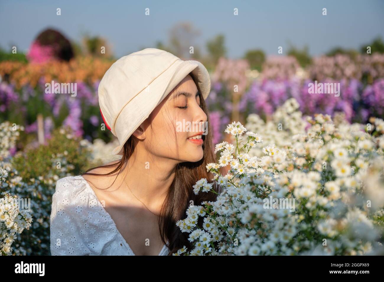 Schöne junge asiatische Frau trägt Hut riechende Cutter Blume blüht im Garten Stockfoto