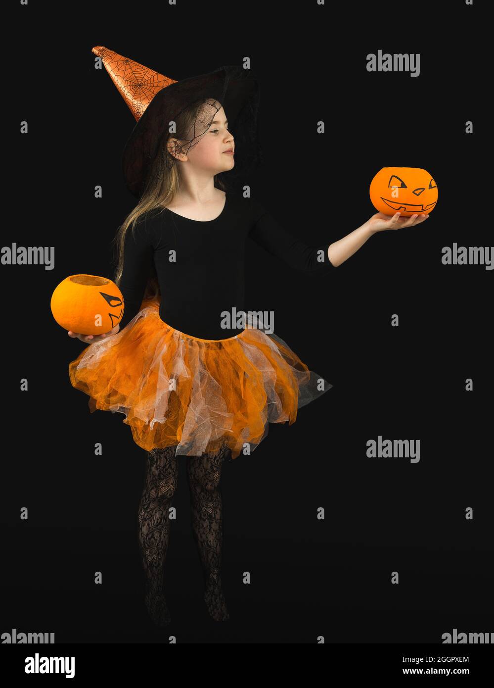 Ein lustiges Mädchen mit langen Haaren mit zwei Jack Kürbissen und in einem Hexenkostüm für Halloween Feier. Orangefarbener Hut und Rock, schwarze Bluse, Spinnennetz Stockfoto