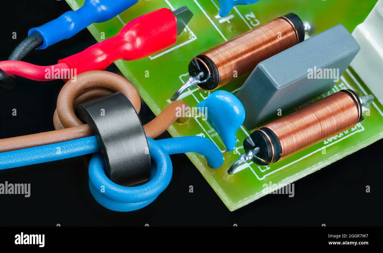 Leiterplattendetails mit Induktivitäten oder Kondensatoren auf schwarzem Hintergrund. Elektronische Bauteile - Ferritperlen, isolierte Drähte, Spulen oder Faston-Klemmen. Stockfoto