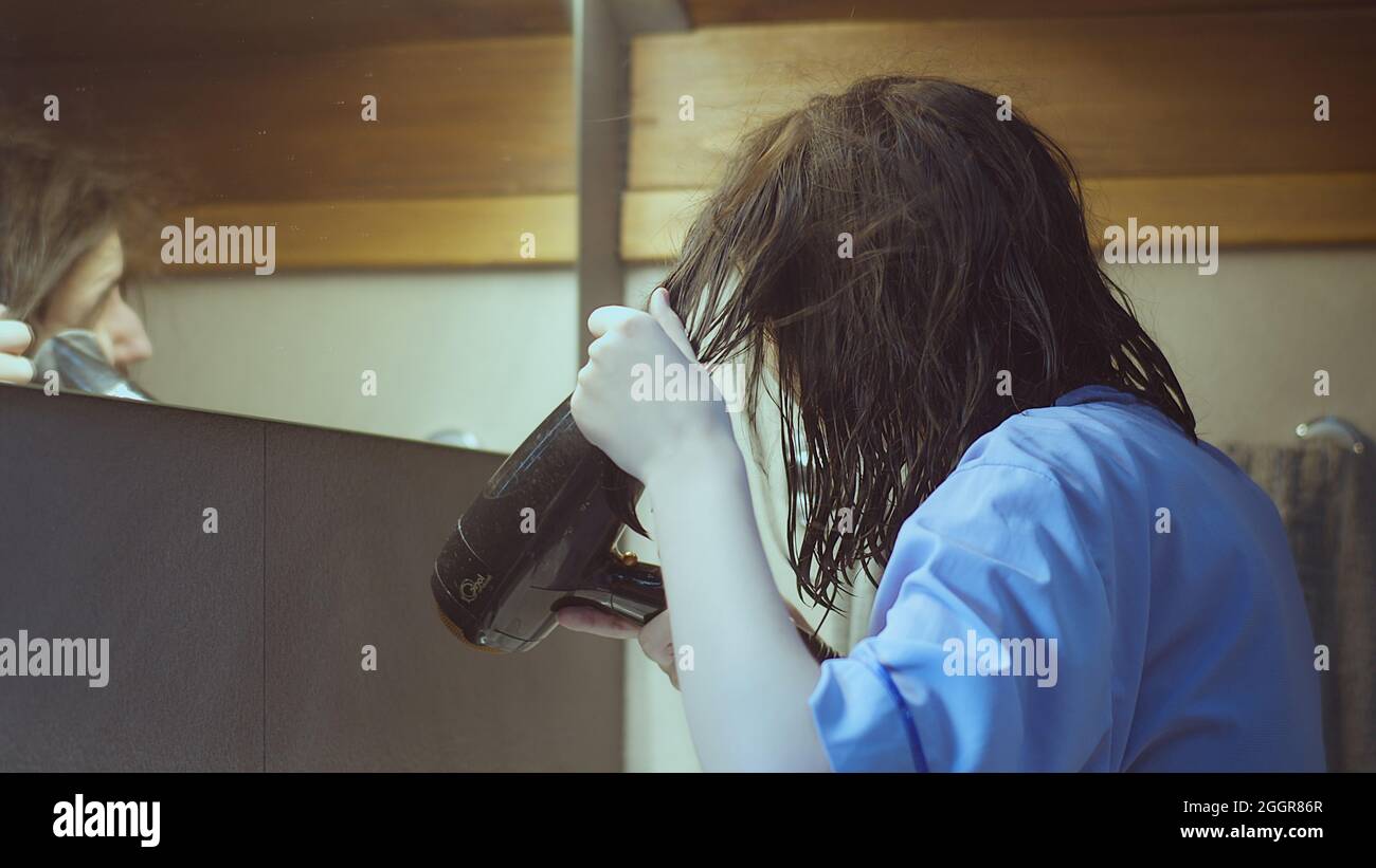 Das Teenager-Mädchen im Badezimmer trocknet ihre Haare nach der Dusche mit einem Haartrockner Stockfoto