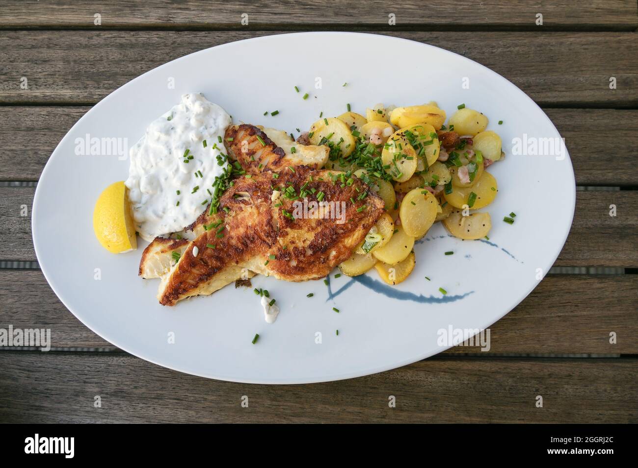 Saftig geröstetes Rotbarsch-Filet mit Bratkartoffeln und Remoulade-Dip auf einem Teller und auf einem rustikalen Holztisch, Blick von oben Stockfoto