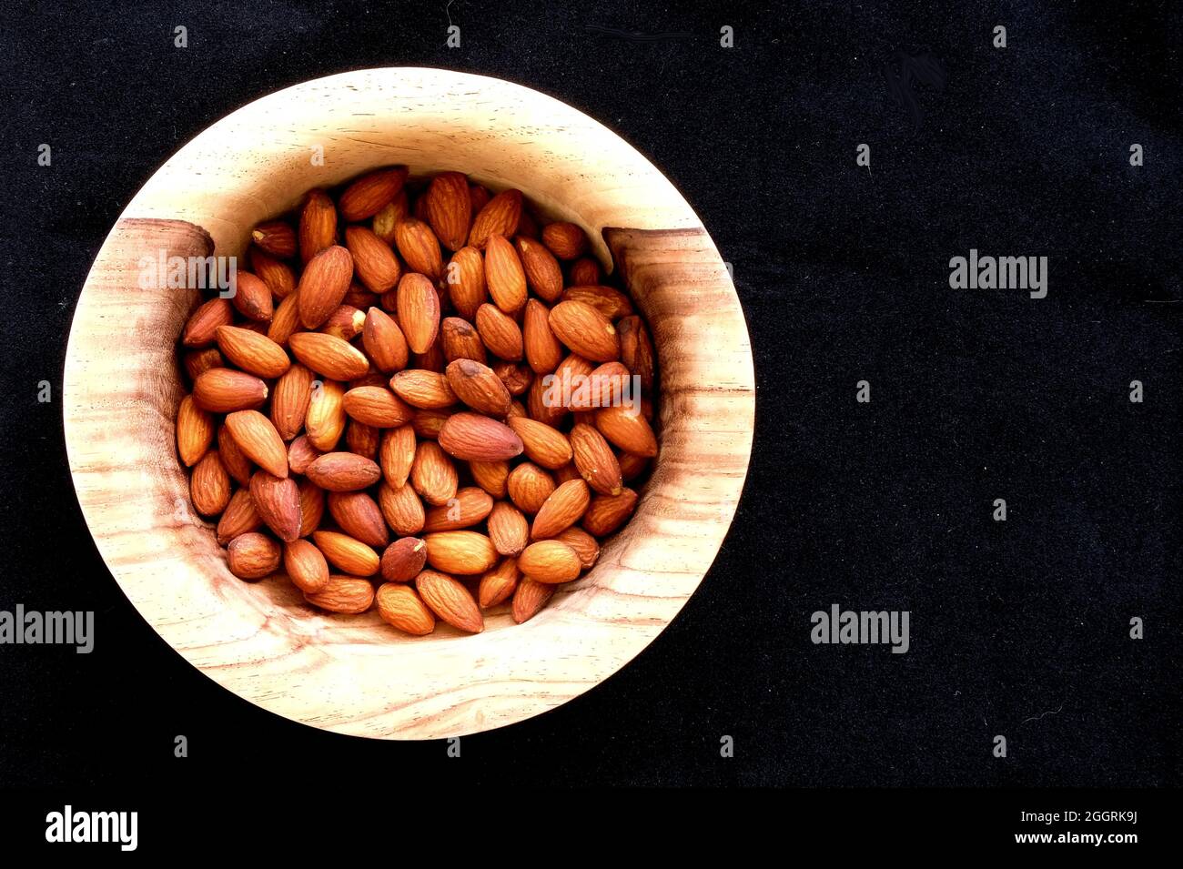 Trocken geröstete Mandeln in einer Holzschüssel von oben auf schwarzem Hintergrund gesehen; gesalzene Snacks für Protein und eine gesunde Ernährung. Stockfoto
