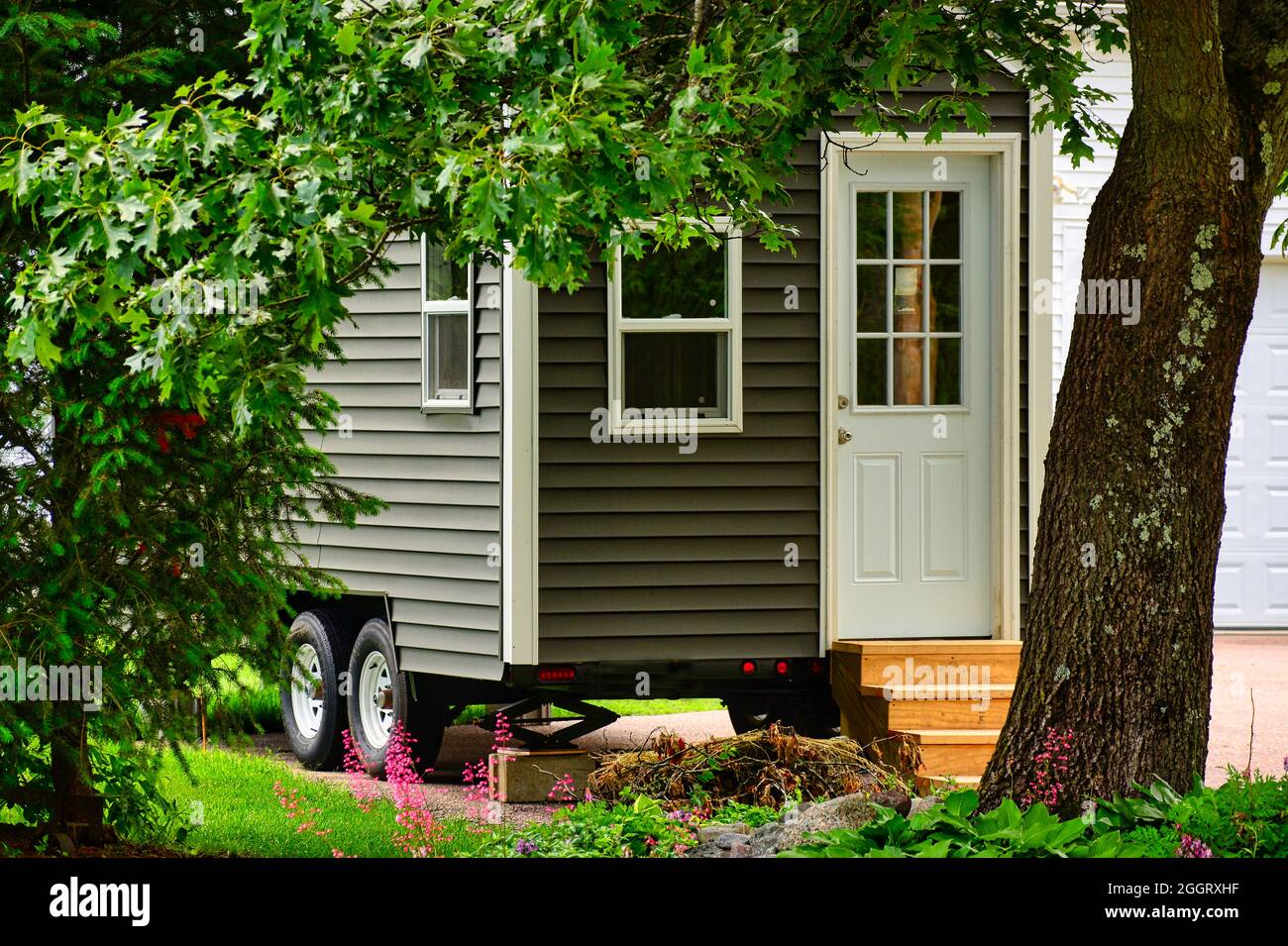 Winziges Haus auf Rädern, eingerahmt von Bäumen und Blumen Stockfoto