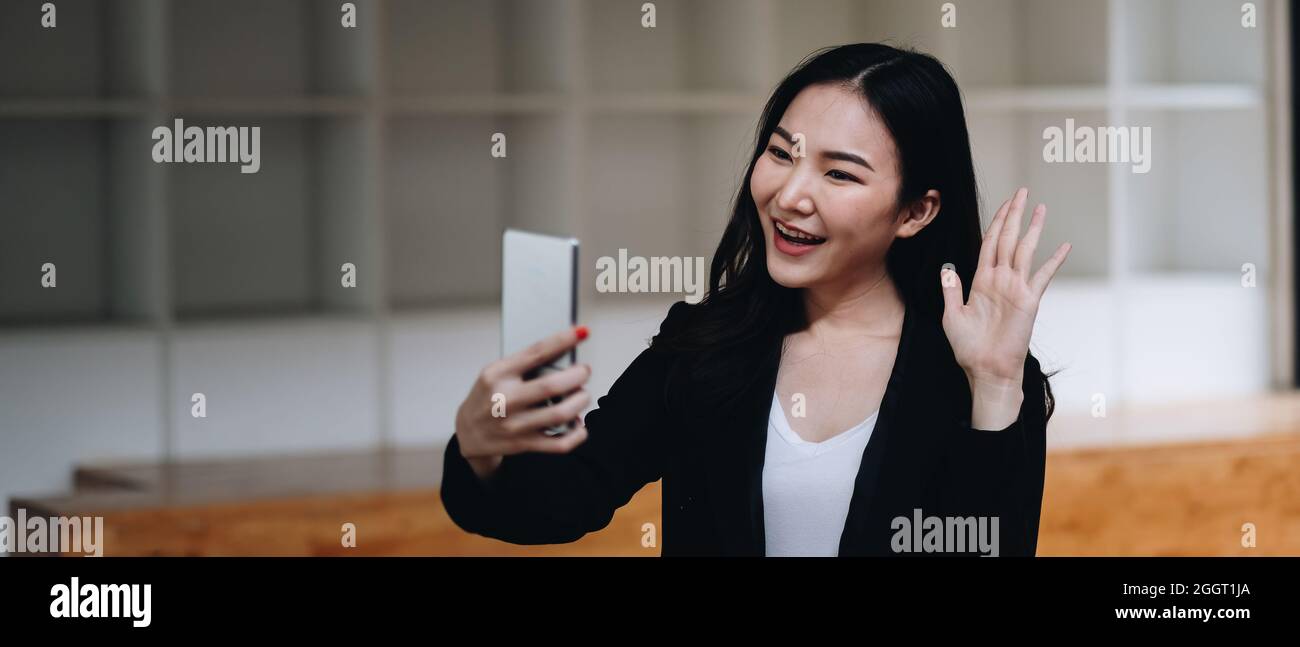 Glückliche junge asiatische Frau hält Telefon Blick auf den Bildschirm winkende Hand Video Anruf Distanz Freund online in mobilen Chat-App mit Smartphone-Videochat Stockfoto