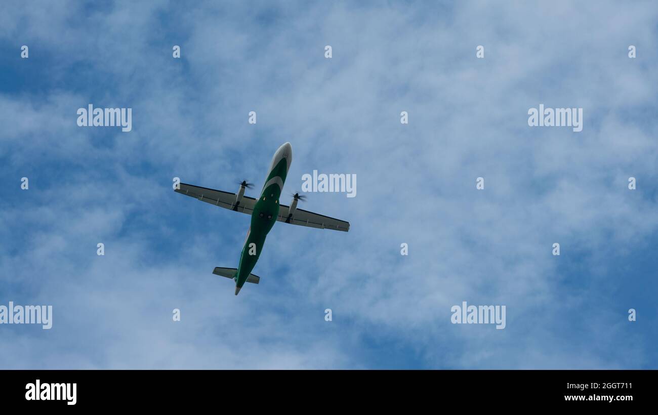 Ein Propellerflugzeug für zivile Passagiere, das über den Kopf fliegt. Jet-Flugzeug, das tief mit blauem Himmel und Wolken im Hintergrund fliegt. Flugzeug fliegen in Tag ti Stockfoto