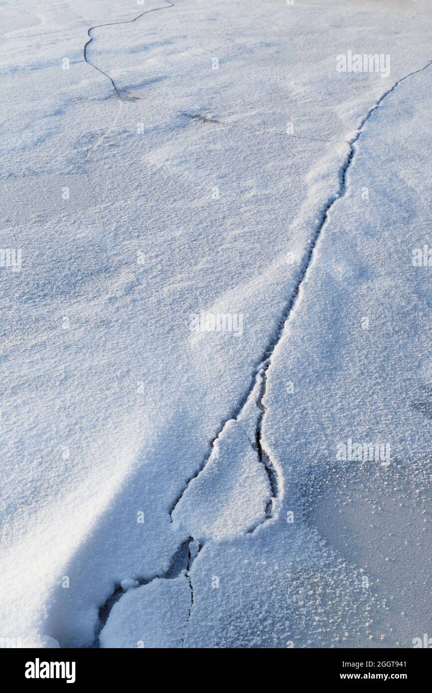 Schnee auf rissem Eis auf einem gefrorenen See im Winter. Abstrakter strukturierter Hintergrund im Vollformat. Speicherplatz kopieren. Stockfoto