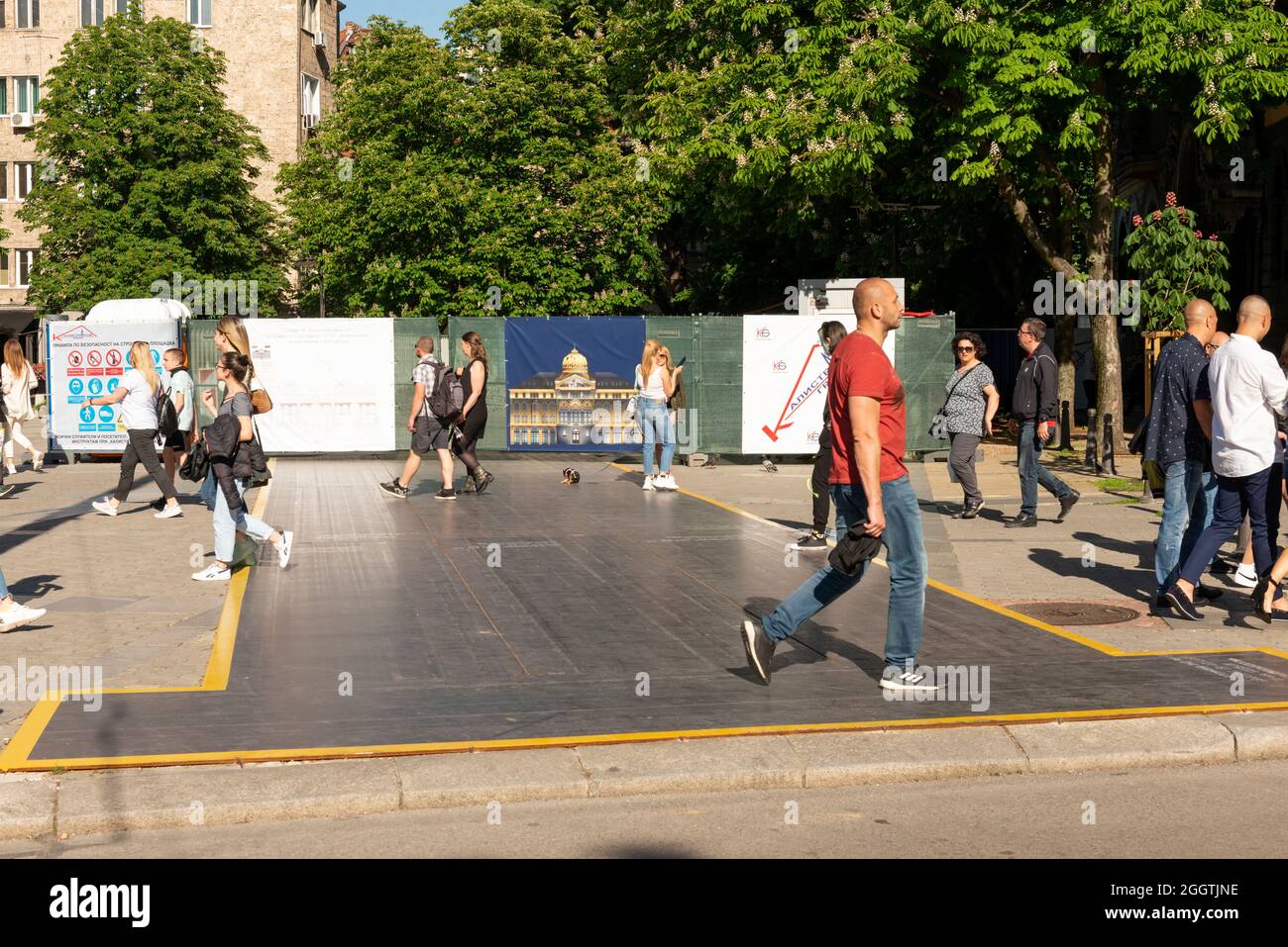 Personen, die auf einem Edelstahlblech als temporärer Schutz der Trittfläche auf dem Bürgersteig für eine Baustelle in städtischer Umgebung laufen Stockfoto