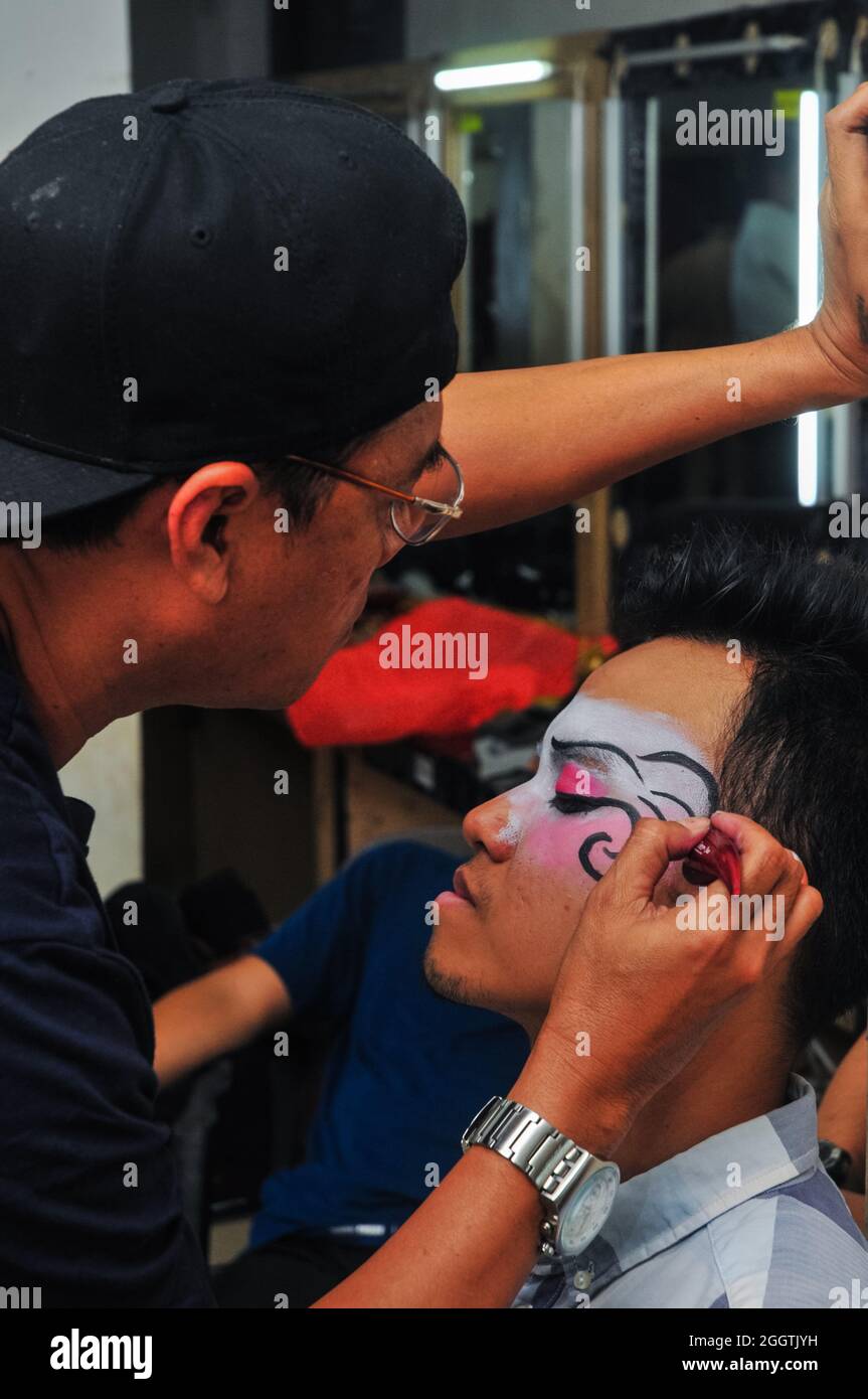 Ein Make-up-Künstler zeichnet ein Motiv auf das Gesicht einer Tänzerin, die auf der Bühne auftreten wird. Stockfoto