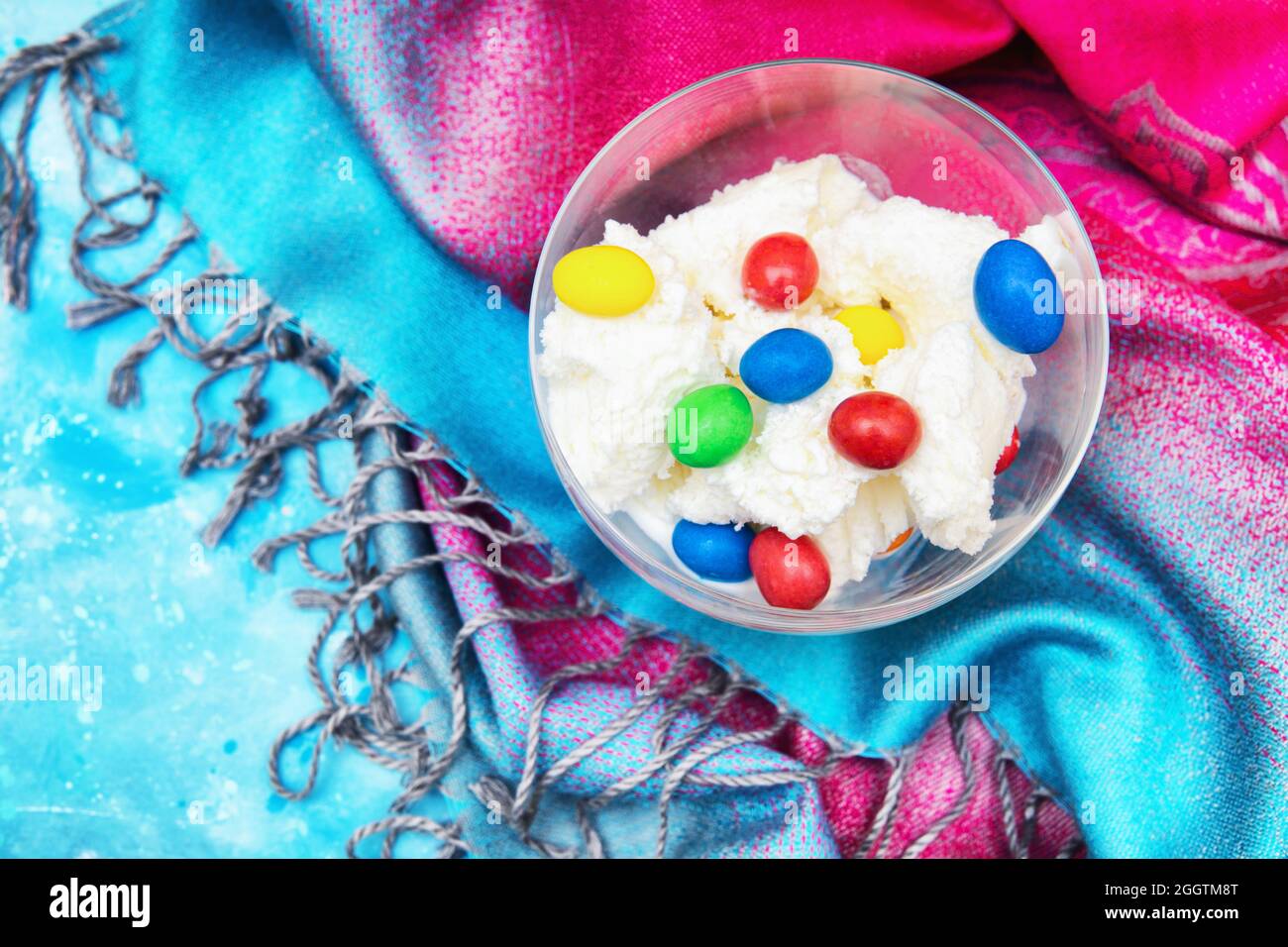 Glasschale mit Eiscreme und farbigen Süßigkeitendragees auf einem farbenfrohen Stoffhintergrund Stockfoto