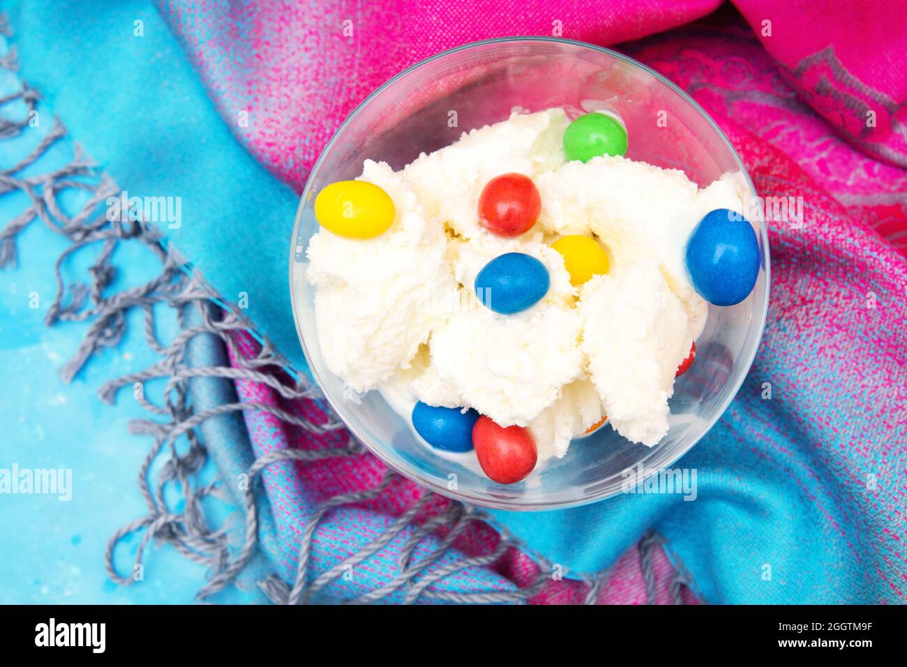 Nahaufnahme einer Glasschüssel mit Eis und farbigen Süßigkeitendragees auf einem farbenfrohen Stoffhintergrund Stockfoto