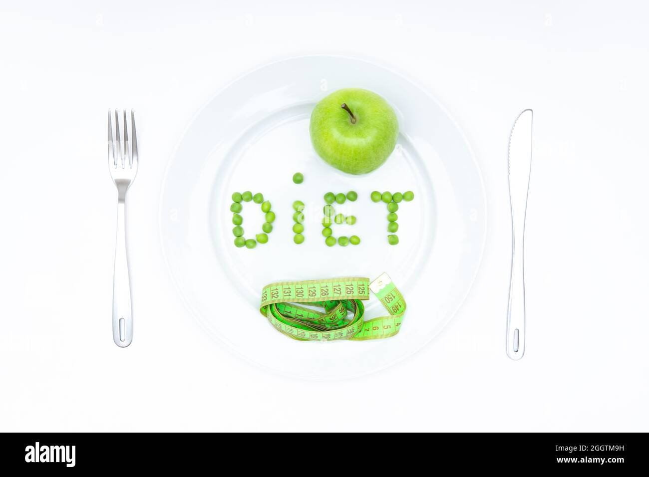 Wort DIÄT aus Gartenerbsen angeordnet und serviert auf einem großen weißen Teller mit einem frischen grünen Apfel, ein weiches Maßband, Messer und Gabel isoliert auf weiß. Stockfoto