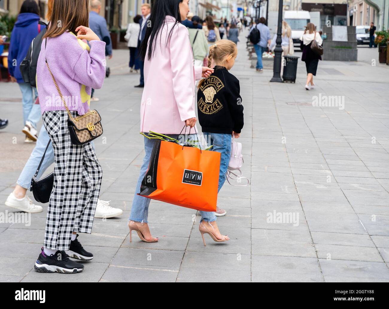 Eine Frau, die eine Einkaufstasche des TSUM-Kaufhauses trägt, geht mit der Familie, die stilvoll in Branded-Outfits gekleidet ist, durch Moskau, Russland. Konzept-Konsum. Stockfoto