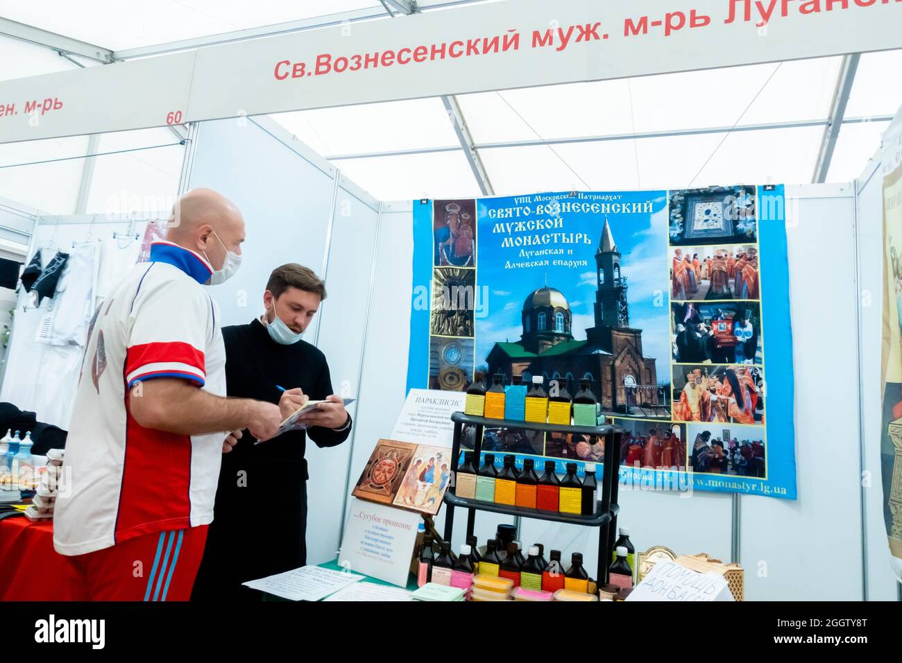 Männlicher Klostervertreter, der an einem Kunden in Sportuniform am Stand auf der orthodoxen Messe in Moskau, Russland, teilnahm Stockfoto