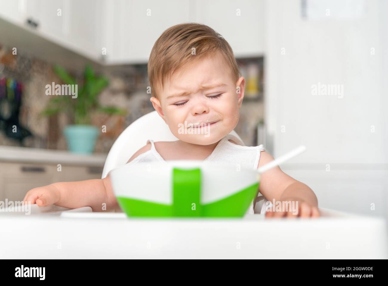 Unglücklicher kleiner kaukasischer Junge mit schmutzigem, unordentliches Gesicht, der auf einem Hochstuhl sitzt. Baby weint, launisch, weigert euch zu essen Stockfoto