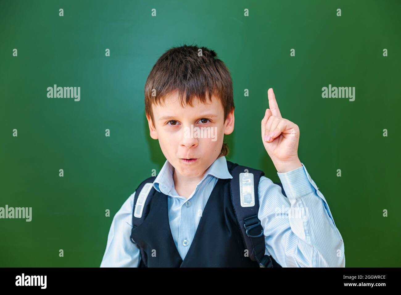 Lustige Schuljunge Grimassen in der Nähe der grünen Schultafel im Klassenzimmer. Grundschulkind mit Tasche. Zurück zur Schule. Stockfoto