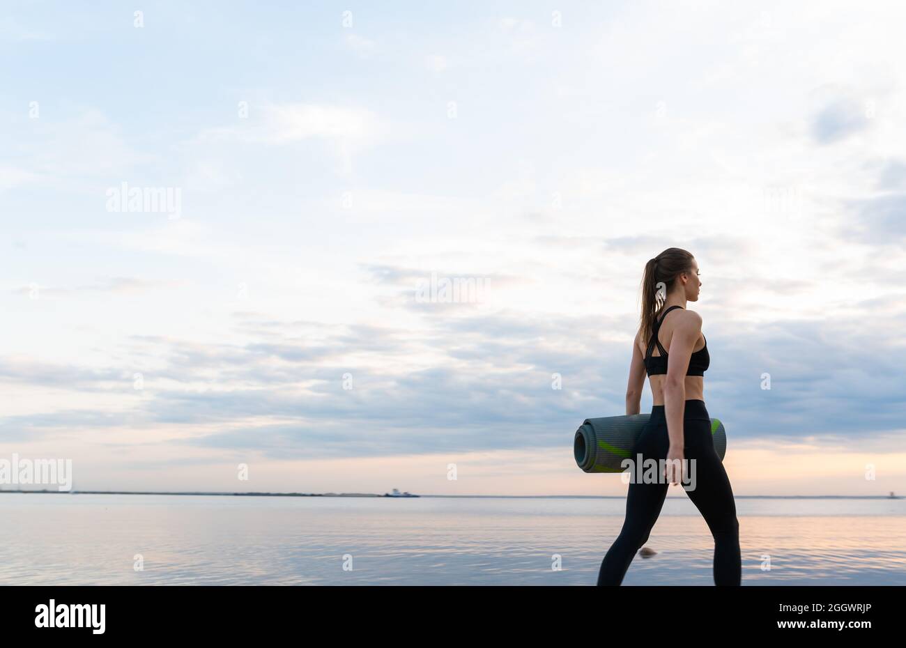Das junge Fitnessmodell mit Yogamatte lässt bei Sonnenuntergang gegen den Himmel Stockfoto