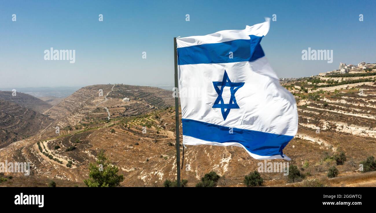 Israelische Flagge auf dem Hintergrund von Judäa und Samaria. Sonniger Tag mit Blick auf seltene Siedlungen in der Wüste Stockfoto