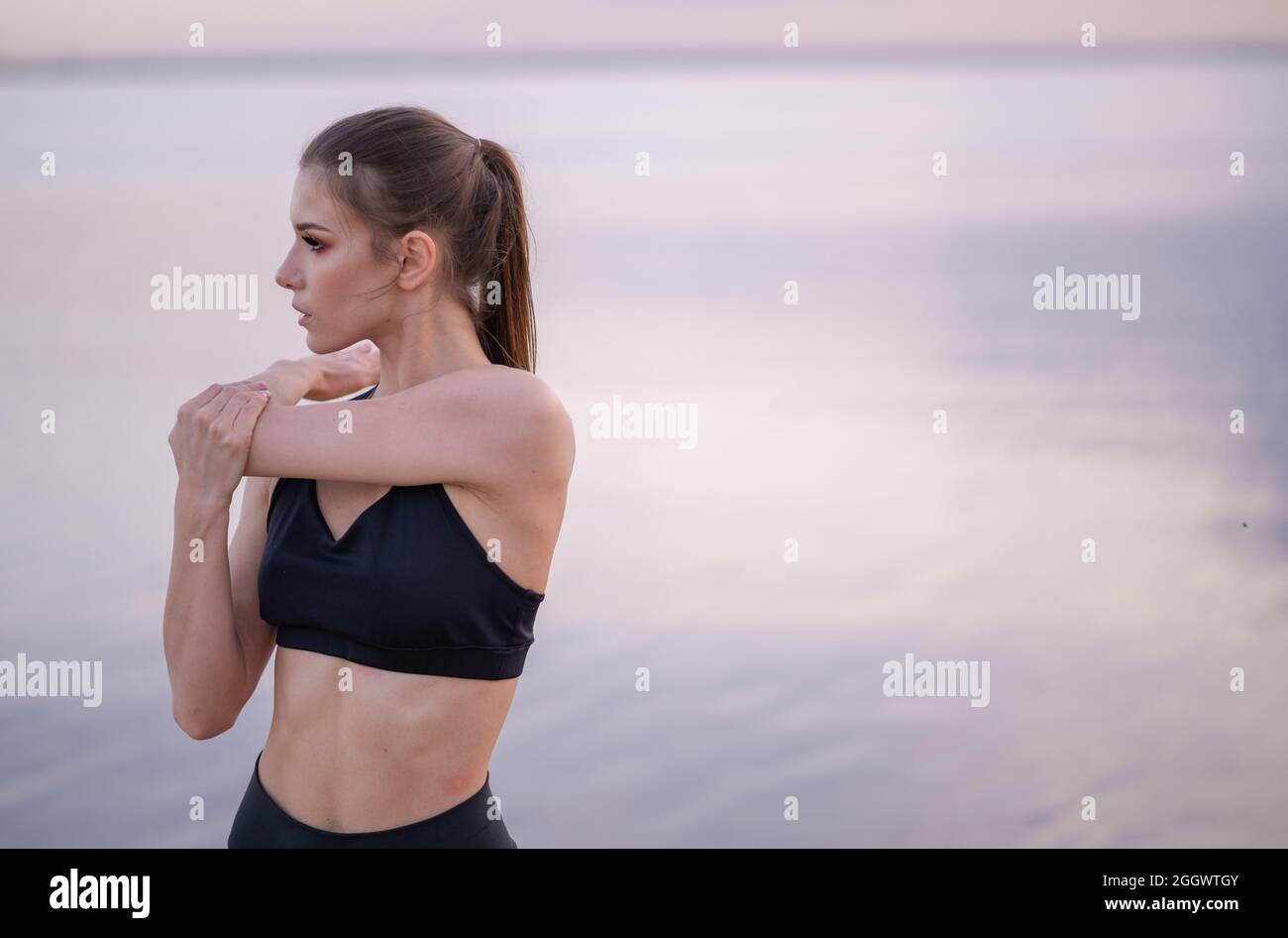 Junges Mädchen in Fitness-Kleidung am Meer führt Übungen Stockfoto