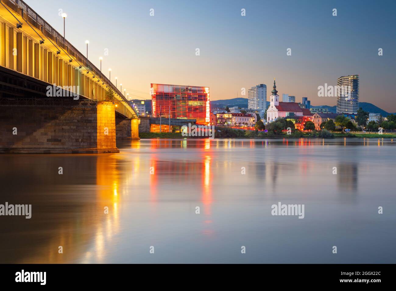 Linz, Österreich. Stadtbild des Flussufers Linz, Österreich bei Sonnenuntergang im Sommer mit Spiegelung der Lichter der Stadt in der Donau. Stockfoto