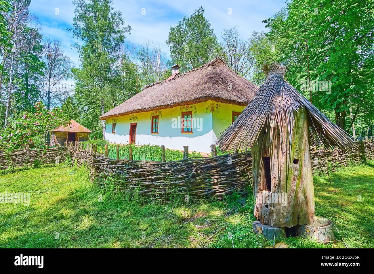 Das kleine, weiß getünchte Haus der Imkerin mit Blumenschmuck, Strohdach, Weidenzaun und dem Blockhaus im Vordergrund, Pereiaslav Stockfoto