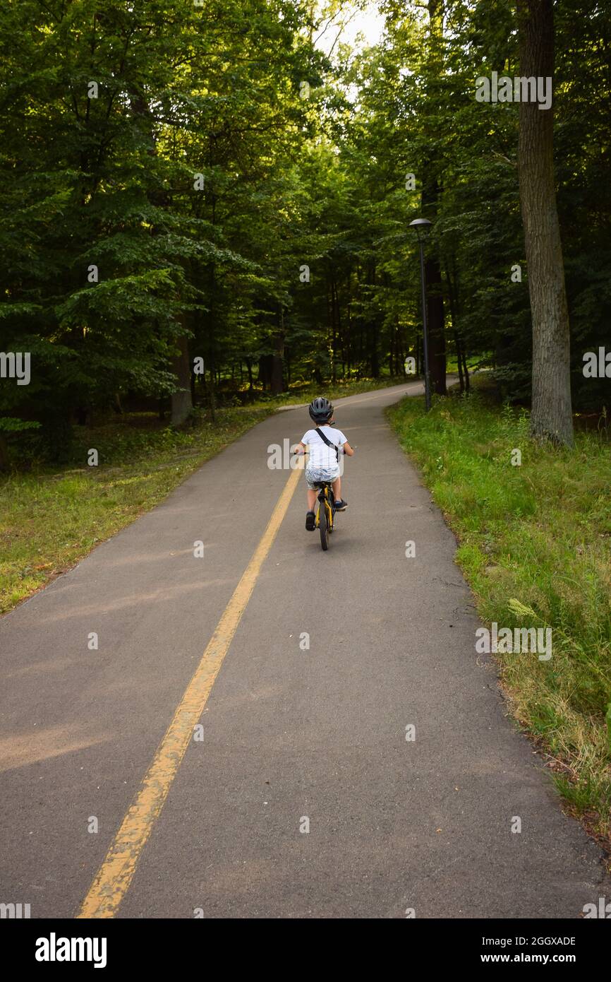 Ein Junge auf einem Fahrrad und mit einem Helm fährt allein auf einem Asphaltweg im Park Stockfoto