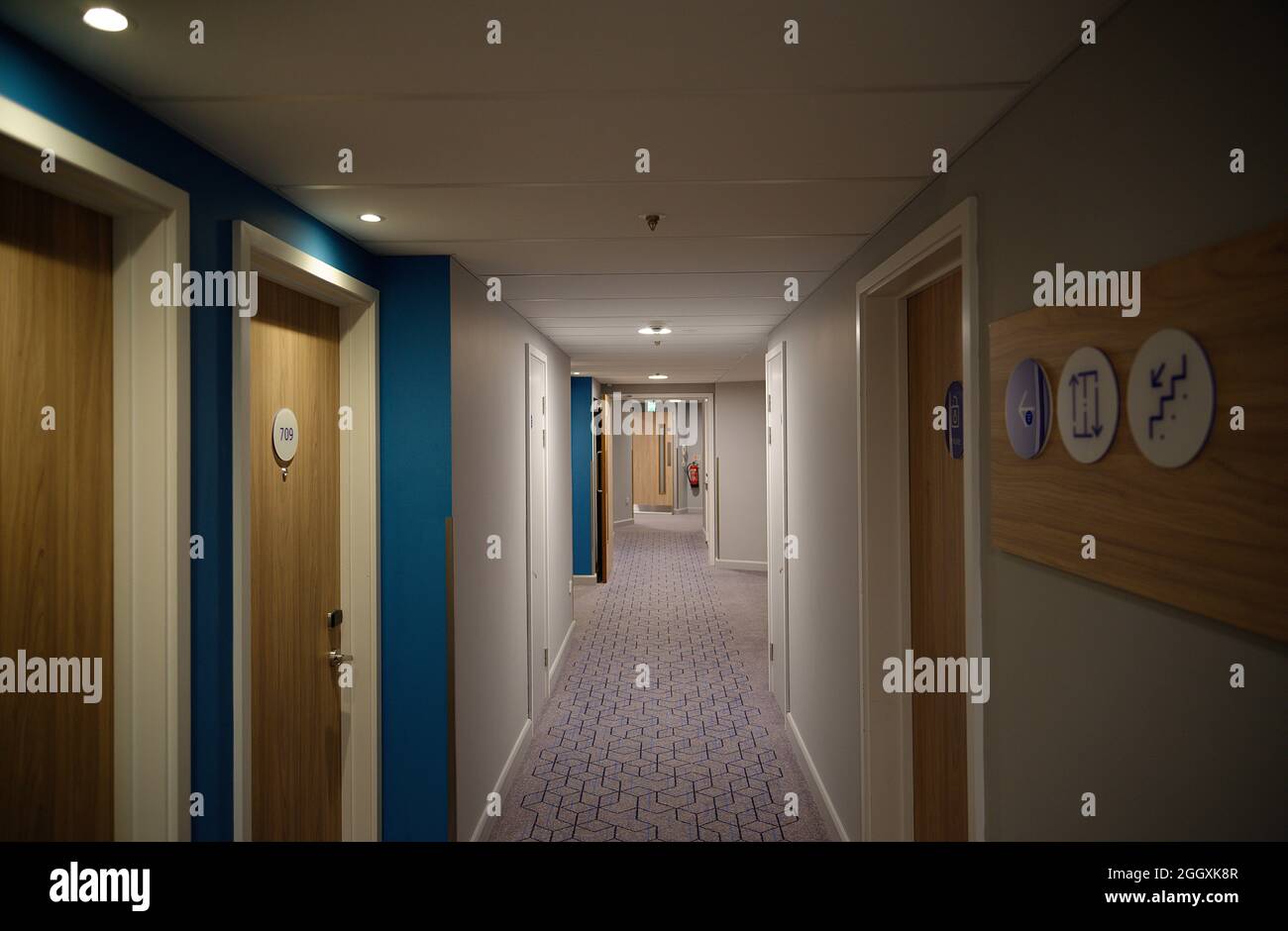 Ein schwach beleuchteter Hotelkorridor mit schlichten Wänden und einem gemusterten Teppich. Stockfoto