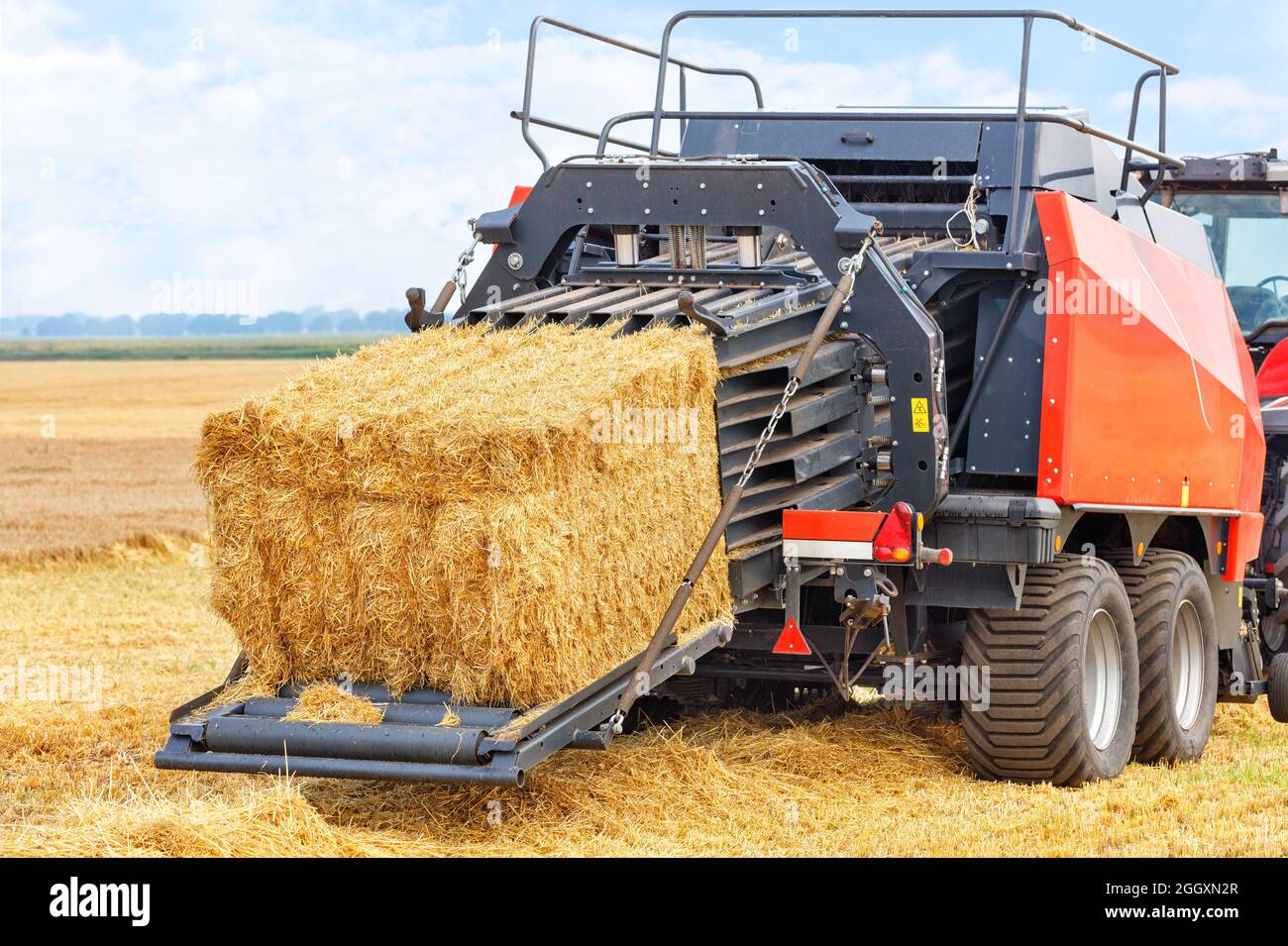 Während der Ernte bildet ein Traktor in einem Weizenfeld mithilfe einer Anhängeeinheit Strohscheiben zu dichten Briketts. Nahaufnahme, Kopierbereich. Stockfoto