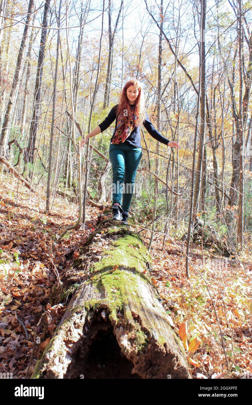 Rothaarige Frau, die auf einem Holzbalken im Wald in den Bergen läuft und versucht, das Gleichgewicht zu finden Stockfoto
