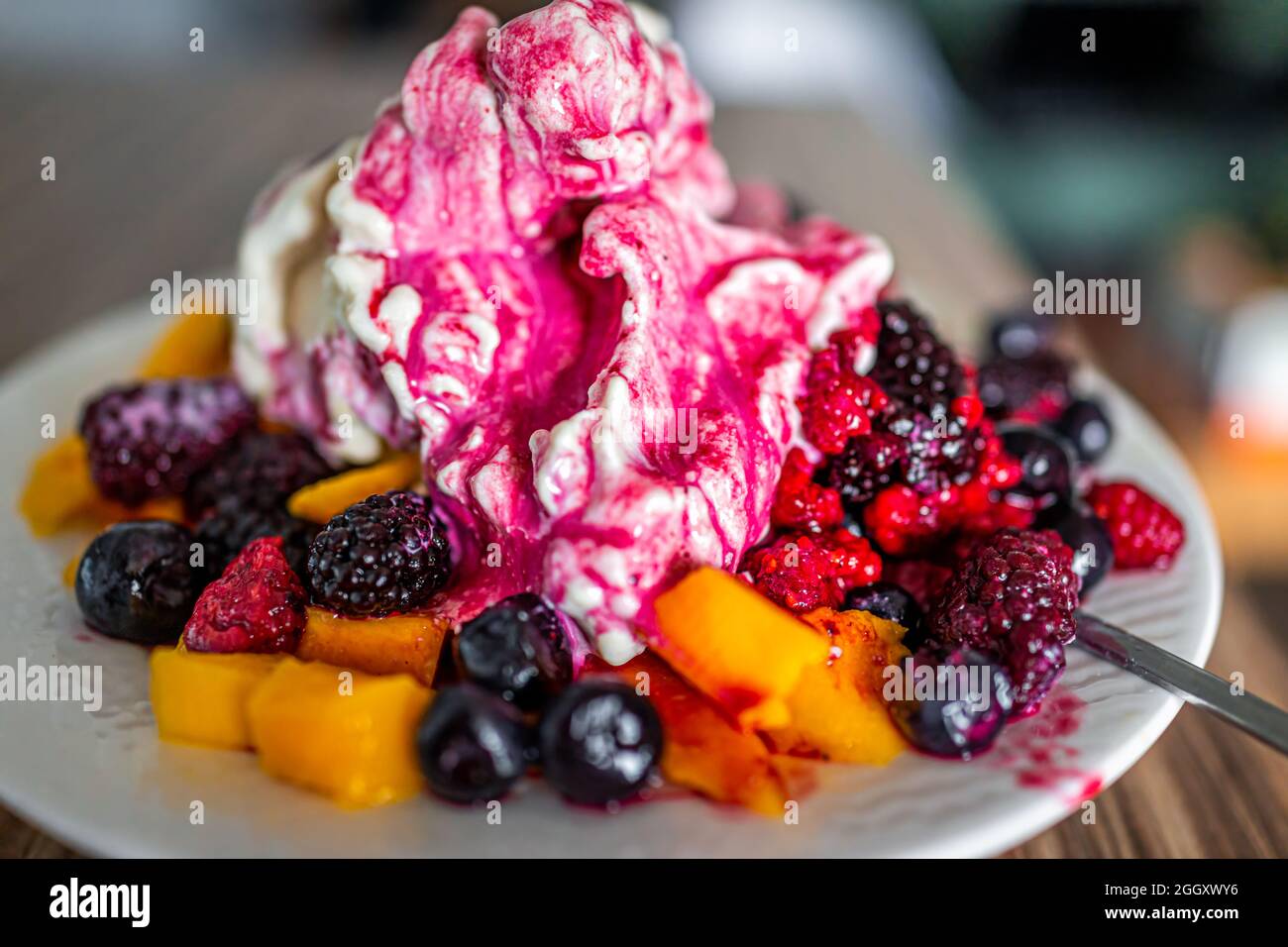 Makro-Nahaufnahme von bunten Schüssel weißen Teller Vanillebanane veganes Eis mit gefrorenen Heidelbeeren, roten Himbeeren und Mango mit sp gekrönt Stockfoto