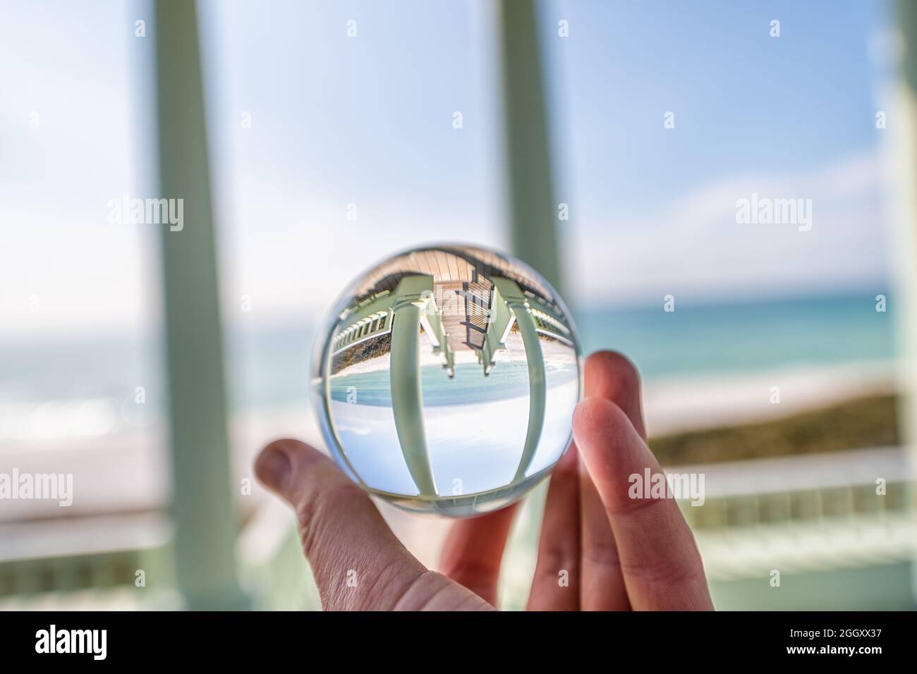 Seaside, Florida mit Hand halten Lensball Kristall Glaskugel mit Reflexion der grünen hölzernen Pavillon Pavillon Architektur am Strand Ozean in verschwommen b Stockfoto