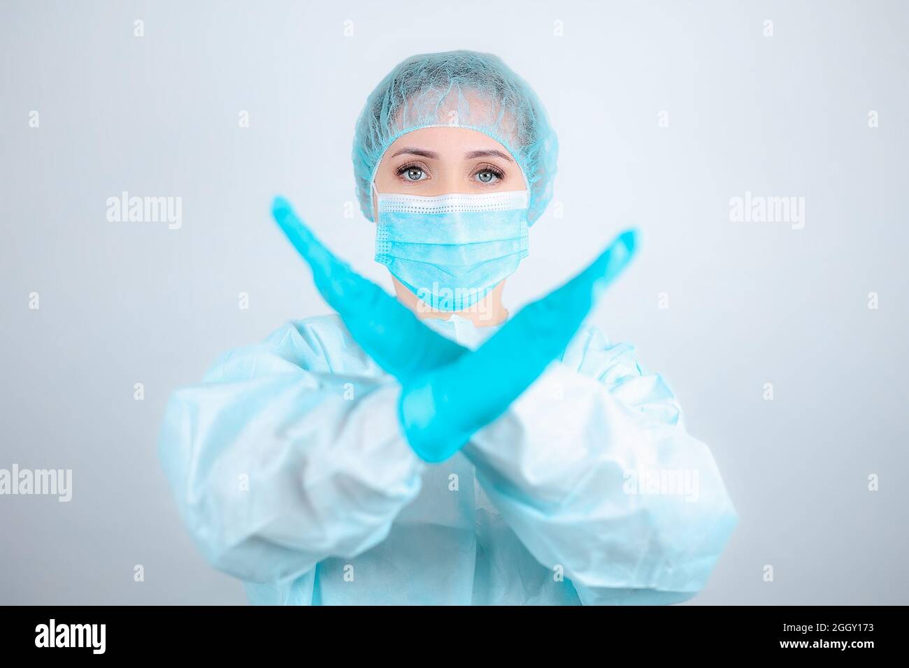 Eine Krankenschwester in einem medizinischen Gewand, einer Maske und Schutzhandschuhen steht aufrecht mit gekreuzten Armen vor ihr Stockfoto