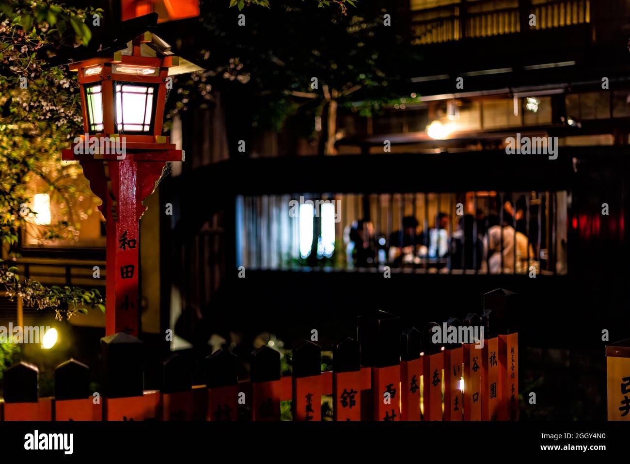 Kyoto, Japan - 16. April 2019: Gion-Viertel mit Kirschbäumen im Gartenpark und roter Laterne in der Nacht am Fluss und Hintergrund eines gehobenen Restaurants Stockfoto