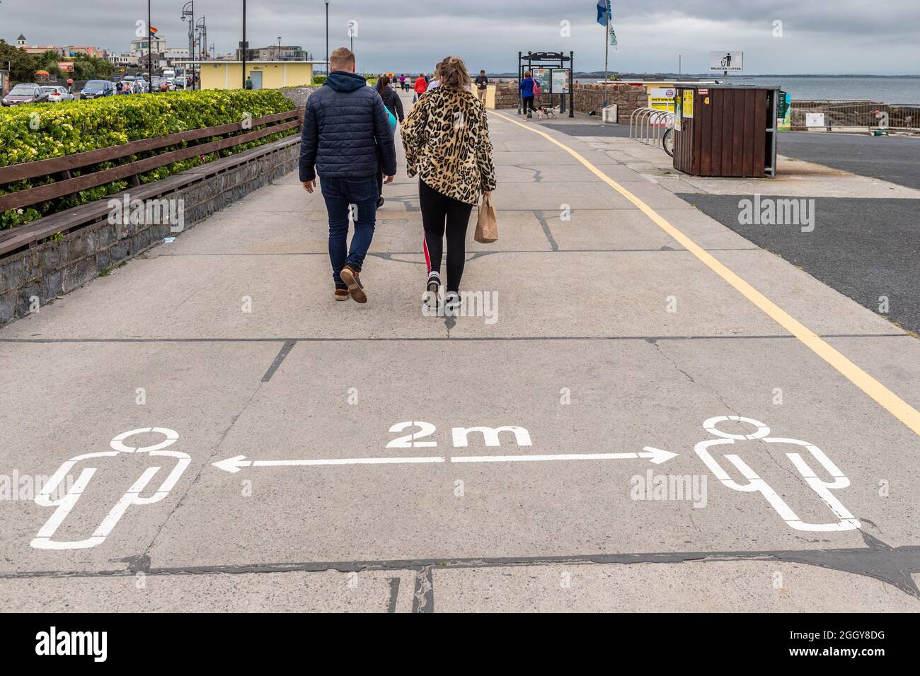 Die Menschen gehen an einem COVID-19 2m Schild an der Promenade in Salthill, County Galway, Irland, vorbei. Stockfoto