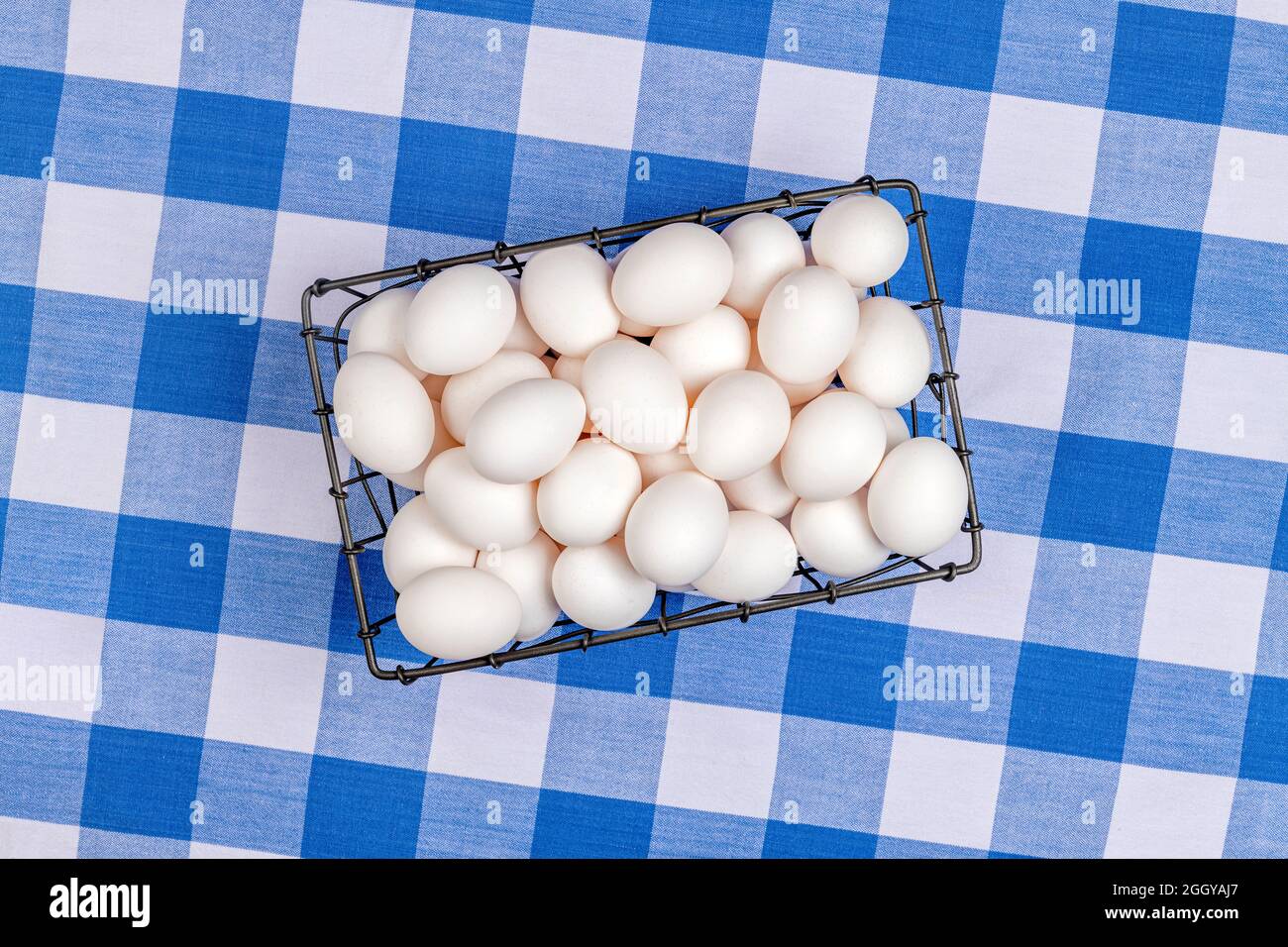 Eine kleine Kiste mit frischen Eiern liegt auf einer Tischplatte, die mit einer traditionellen, blau-weiß karierten Tischdecke bedeckt ist. Stockfoto