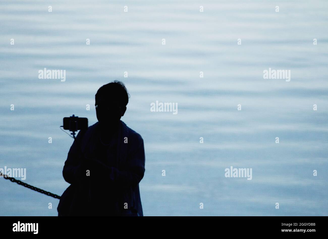 Silhouette einer Frau, die in der Abenddämmerung das Wasser fotografiert, Victoria BC, Kanada. Stockfoto