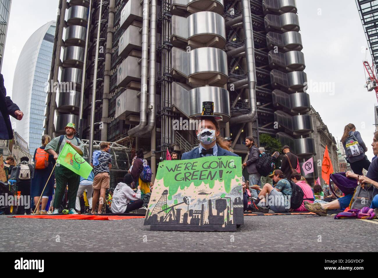 London, Großbritannien. September 2021. Ein Protestler in einem Kostüm sitzt auf der Straße mit dem „Wir werden grün!“ Plakat während der Demonstration vor Lloyd's of London. Extinction Rebellion Demonstranten marschierten in der City of London im Rahmen ihrer zweiwöchigen Kampagne „Impossible Rebellion“ ein und forderten die britische Regierung auf, in der Klima- und Umweltkrise sinnvoll zu handeln. (Foto: Vuk Valcic/SOPA Images/Sipa USA) Quelle: SIPA USA/Alamy Live News Stockfoto