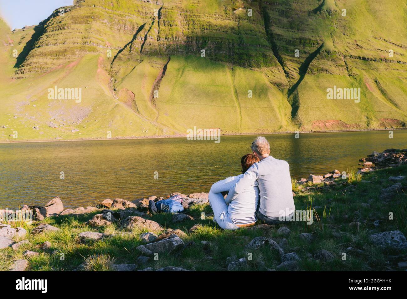 Rückansicht Frau und Mann sitzen in der Nähe des Bergsees und genießen den Blick auf die grünen Hügel - ihr Wanderziel. Reiselebensstil, Fernweh Stockfoto