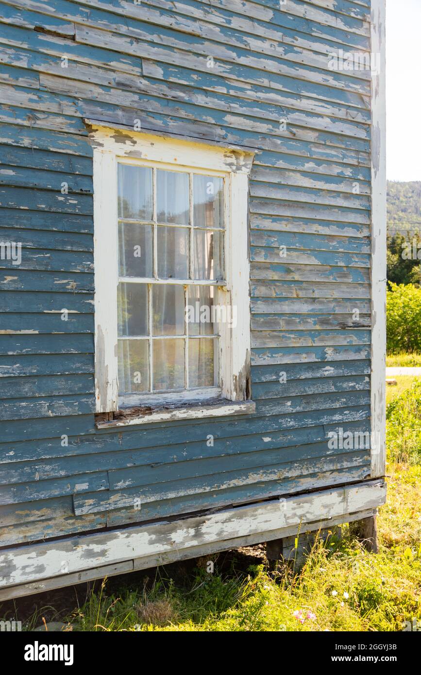 Die Außenwand eines strukturierten, graugrünen, abgenutzten blauen Holzgebäudes. Die Wand hat ein kleines Fenster mit mehreren Glaspaneelen. Stockfoto