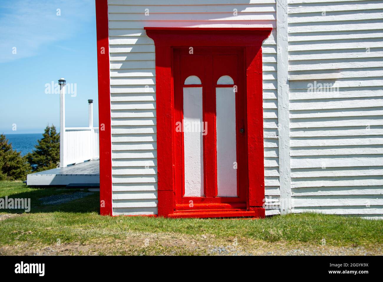 Das Äußere eines alten weißen Holzgebäudes mit leuchtend roten Zierleisten. Es gibt eine alte Holztür mit roten Zierleisten. Das Haus verfügt über eine Terrasse mit Aussicht. Stockfoto
