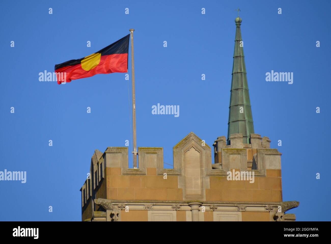 Die rote, gelbe und schwarze Flagge der UreinOriginal First Nations, die auf einem Sandsteingebäude vor dem Hintergrund des blauen Himmels weht Stockfoto