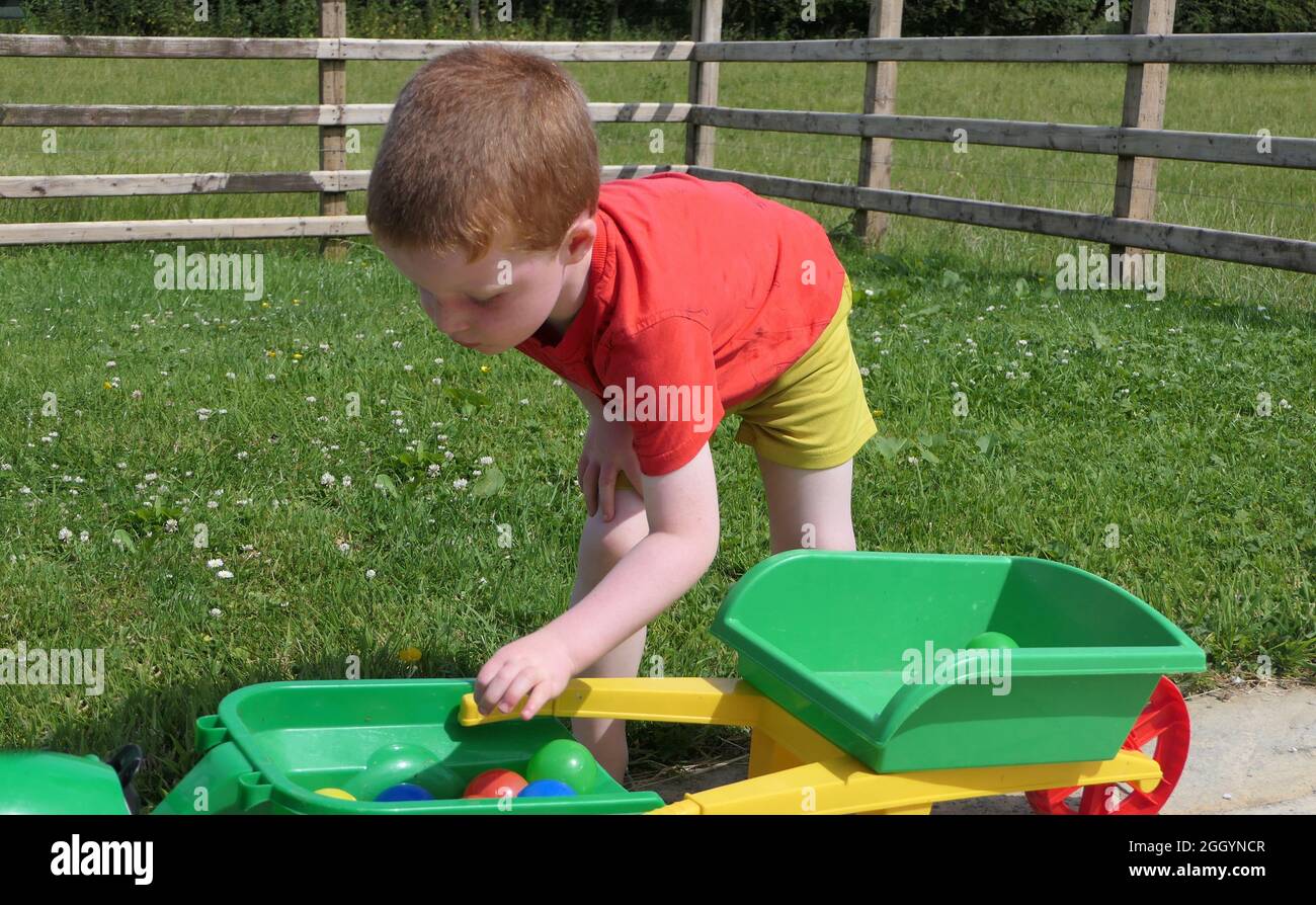 Red headed Child spielt mit Spielzeug in einem Garten Stockfoto