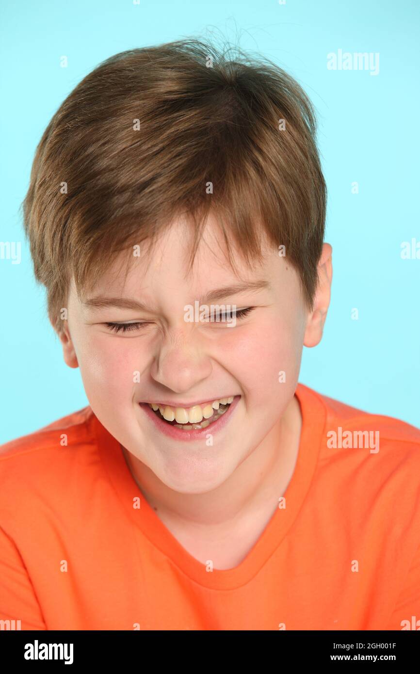 Nahaufnahme-Porträt: Ein gut entwickelter, fröhlicher Teenager in einem orangefarbenen T-Shirt lacht zu Tränen und schließt seine Augen. Stockfoto