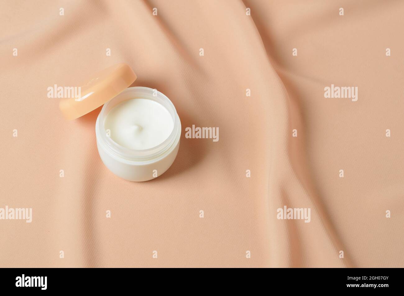 Ein Glas Creme für die Pflege zarter Haut auf einem welligen beigen Hintergrund aus Chiffon. Selektiver Fokus. Stockfoto