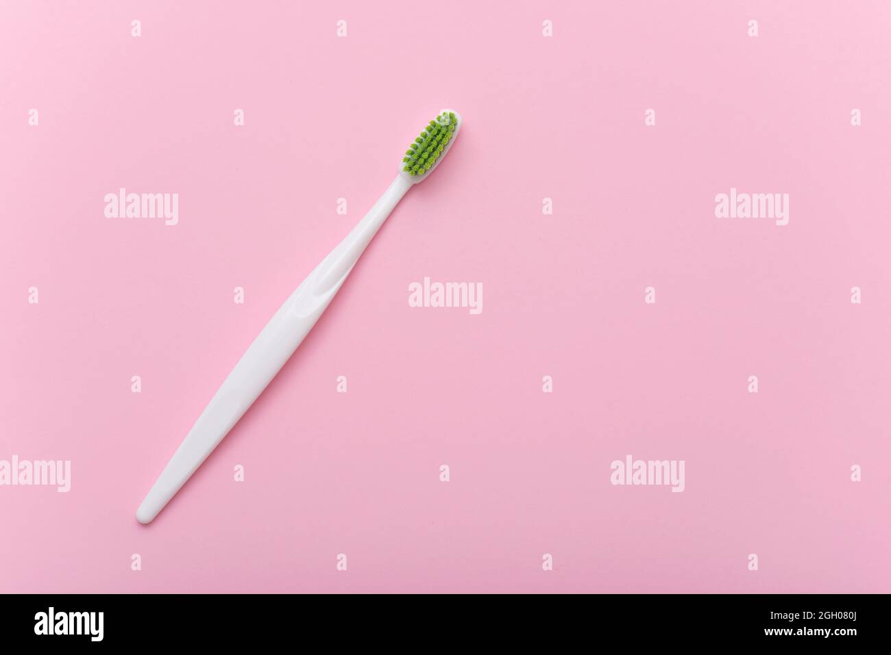 Weiße Plastikzahnbürste mit grünen Borsten als flaches Lay. Zahnbürste auf rosa Oberfläche, Draufsicht, Platz für Text. Stockfoto