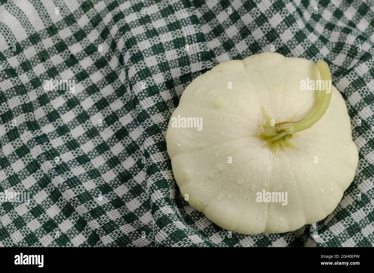 Nahaufnahme eines Pattypan Squash auf der grün karierten Serviette. RAW P Stockfoto